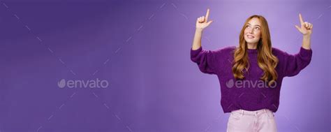 Dreamy girl with red hair and freckles in warm cozy purple sweater raising hands looking and ...