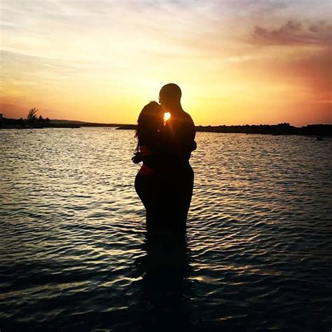 a man and woman are kissing in the water at sunset, with the sun setting behind them