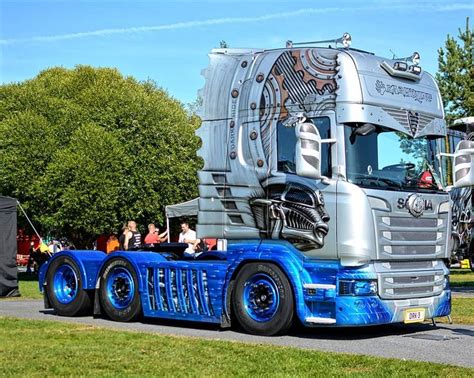 a large semi truck parked on top of a grass covered field next to a forest