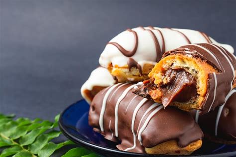 Premium Photo | Eclairs with chocolate filling and white chocolate on black surface.