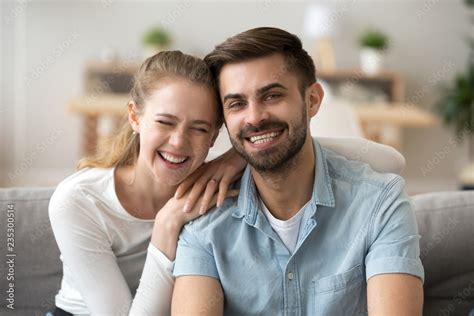 Portrait of smiling young husband and wife hugging sitting on couch ...