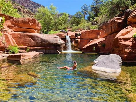 a person swimming in a pool surrounded by red rocks and water falls ...