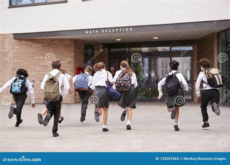 Group of High School Students Wearing Uniform Running into School Building at Beginning of Class ...