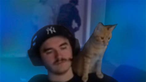 a man wearing a baseball cap with a cat sitting on his shoulder in front of him