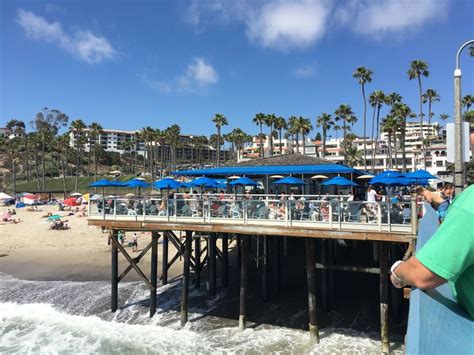 people are standing on the pier near the beach with blue umbrellas and ...