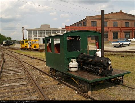 an old green train car sitting on the tracks in front of a building and other buildings