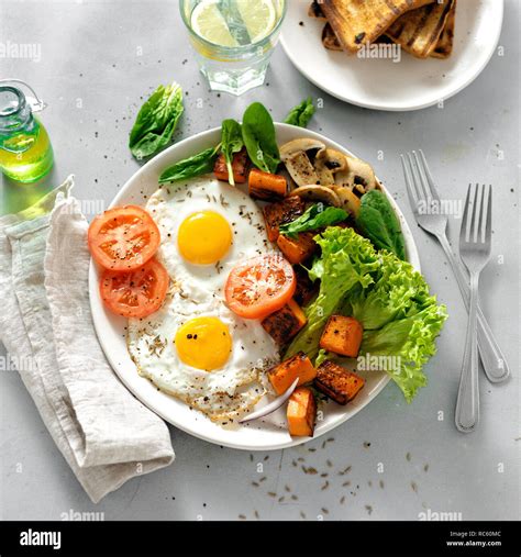 Breakfast table. Breakfast plate with fried eggs, vegetables, mushrooms and toast on gray ...