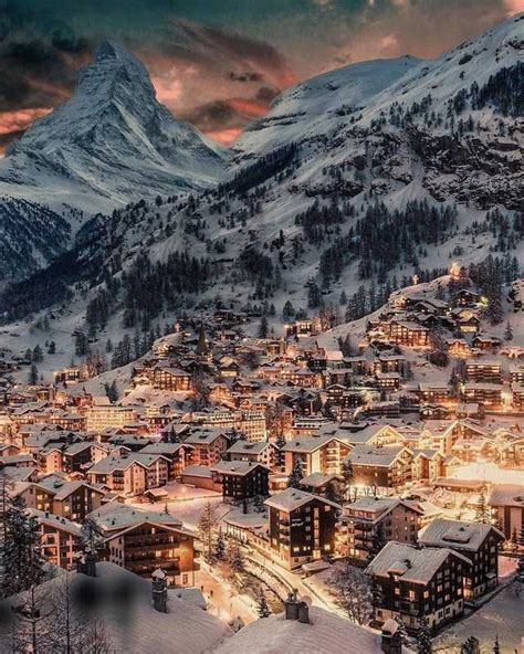 a town in the mountains covered in snow at night with lit up buildings ...