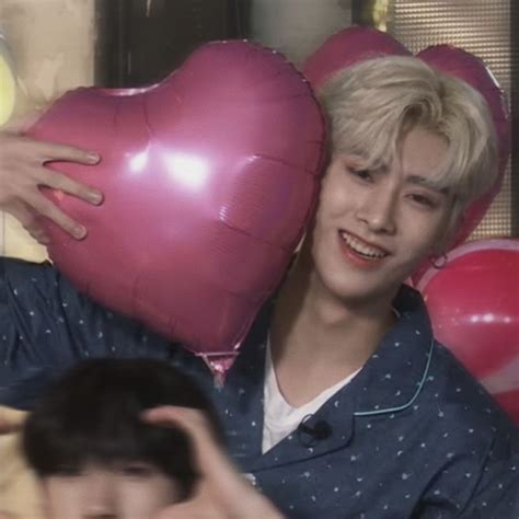 a person holding a heart shaped balloon in front of a wall with balloons behind them