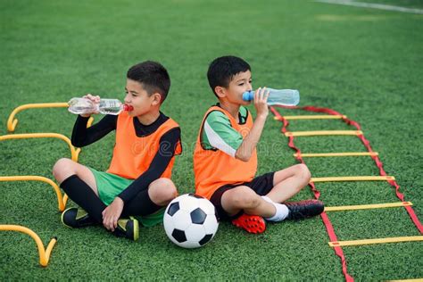 Two Teen Boys in Football Uniforms Having a Rest on Sport Field with Artificial Covering and ...