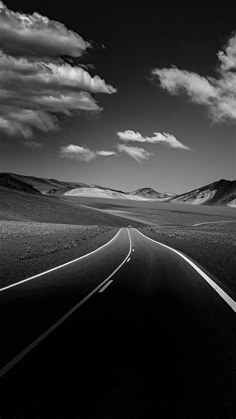 a black and white photo of a road in the middle of nowhere with mountains in the background