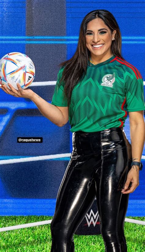 a woman holding a soccer ball in front of a blue wall and green grass area