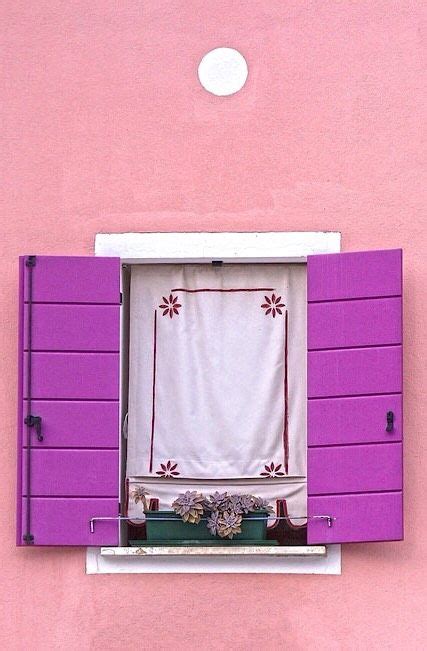 an open window on the side of a pink building with purple shutters and white curtains