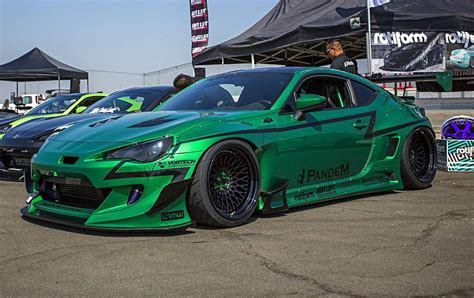 two green sports cars parked next to each other in a parking lot at an auto show