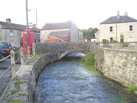 a river running under a stone bridge next to a street with cars parked on the side