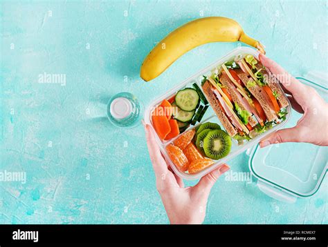 Lunchbox in hands. School lunch box with sandwich, vegetables, water, and fruits on table ...
