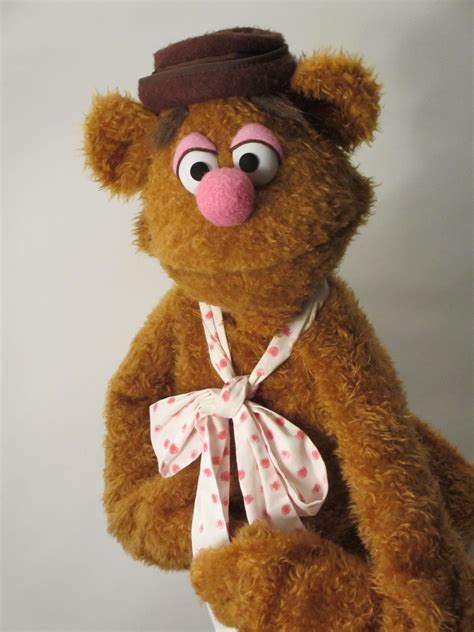 a brown teddy bear wearing a pink polka dot bow tie and a hat with big eyes