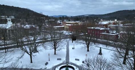 Small park in center of Wellsboro PA. Snow falls on beautiful town in America. Aerial rising ...