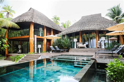 an outdoor swimming pool with chairs and umbrellas next to the water in front of some thatched huts