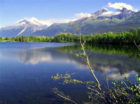 a lake surrounded by mountains and trees in the foreground with blue sky above it