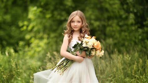 Cute Little Girl With Flowers Is Standing On Green Grass Wearing White ...