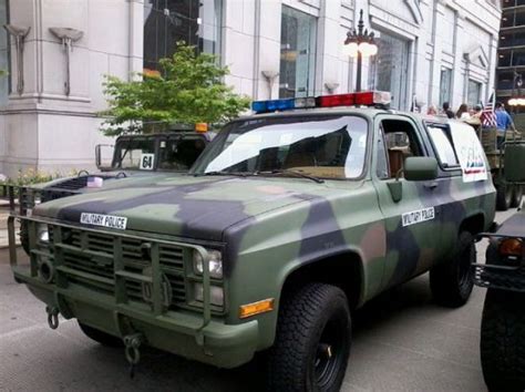 an army truck parked in front of a building with people standing around it on the sidewalk