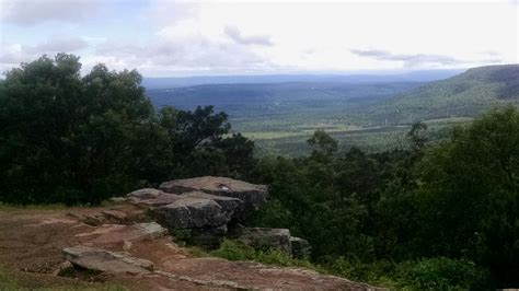 there is a bench on the top of a hill with mountains in the background and trees around it