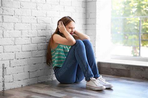 Sad teenage girl sitting near window in a room Stock Photo | Adobe Stock