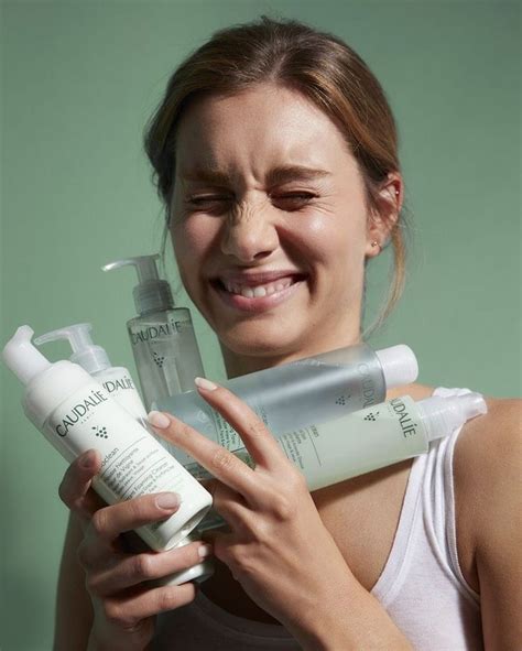 a woman holding two bottles of lotion and a tube of sunscreen on her neck