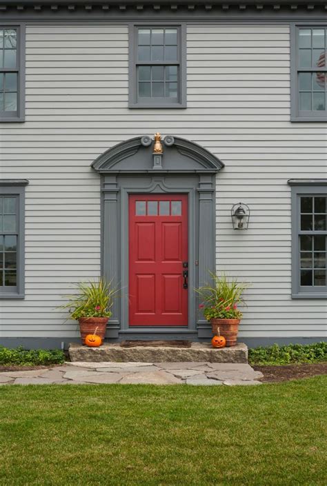 a red door is on the side of a white house with two potted plants