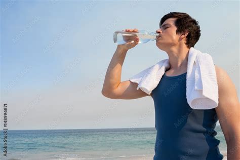 Young man drinking water from bottle at beach Stock Photo | Adobe Stock