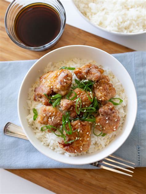 a white bowl filled with rice and meat next to a cup of tea on top of a wooden table