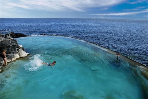 a man swimming in the ocean next to a cliff