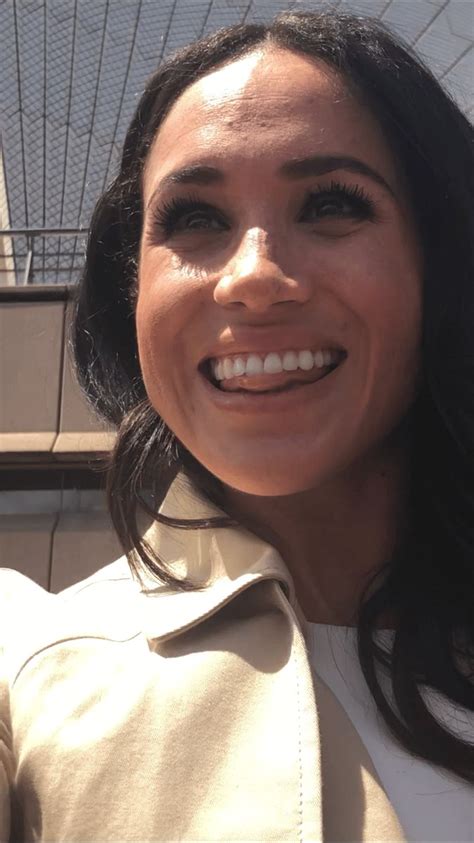 a close up of a person wearing a jacket and smiling at the camera with a building in the background