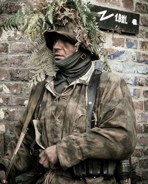 a man in camouflage is standing near a brick wall and wearing a hat ...