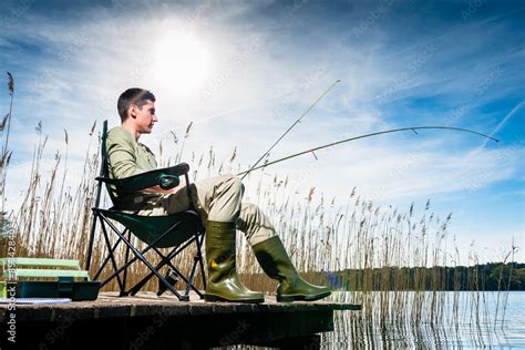 Man fishing at lake sitting on jetty Stock Photo | Adobe Stock