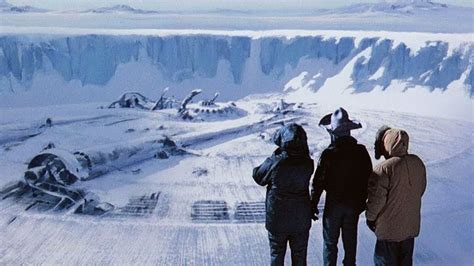 three people standing on top of a snow covered mountain looking out at the mountains below