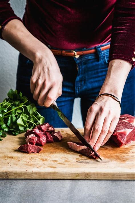 Great food photography / cooking process photography. Woman in a red top cubing beef chuck on a ...