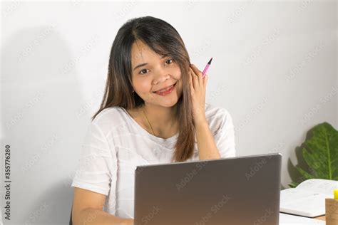 Asian woman wearing white T-shirt Is working happily at home Open the grey notebook screen on ...