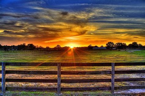 the sun is setting over a field with a wooden fence in front of it,