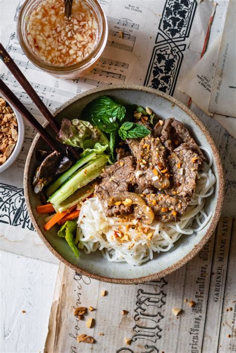 a bowl filled with meat and vegetables next to two bowls of rice, sauce and chopsticks