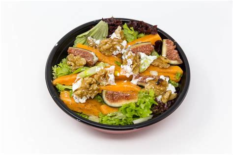 A salat with figs, pumpkin, walnuts and cream cheese in a black bowl ...