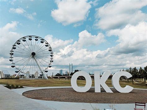 a large white sign that says okc in front of a ferris wheel and park