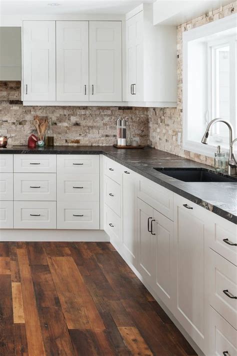 a chic white kitchen with a tan stone tile backsplash and black granite ...