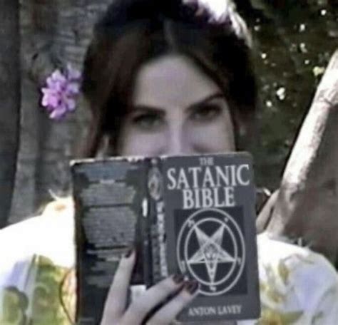 a woman holding up a book with the satanic bible written on it in front ...