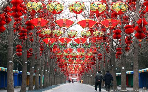 two people walking down a street lined with trees and red lanterns ...