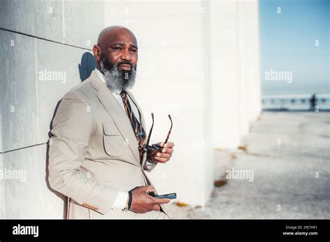 A stylish black man with a bald head and full beard, holding a phone ...