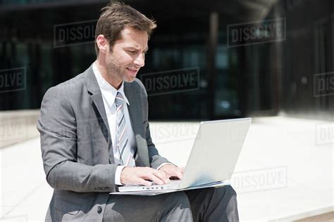 Businessman using laptop outdoors - Stock Photo - Dissolve