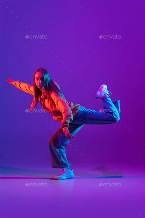 Stylish sportive girl dancing hip-hop in stylish clothes on colorful background at dance hall in ...