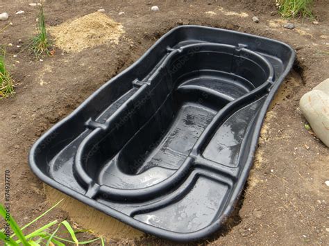 Preformed plastic pond insert installation in a dug stepped hole with sand base in the summer ...